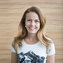Eine lächelnde Frau mit langen, blonden Haaren trägt ein T-Shirt mit Bergmotiv vor einer Holzpaneelwand.