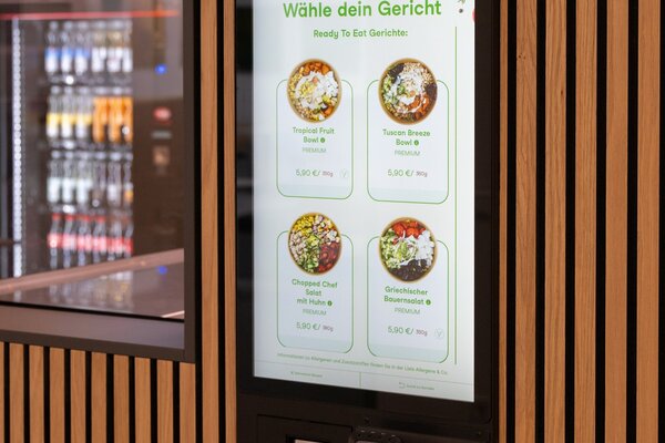 Ein interaktiver Bestellen-Automat bietet eine Auswahl an frischen Gerichten wie Salate und Schalen in einem modernen Umfeld.