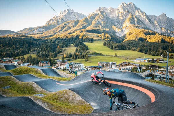 Die Bikestrecke zieht sich durch eine malerische alpine Szenerie, während die Fahrer konzentriert um die Kurven rasen.