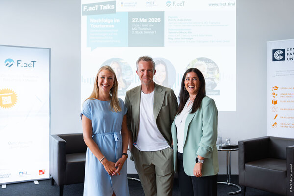 A man and two women pose for a photo, dressed in business attire, in front of a presentation backdrop about tourism.
