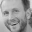 The image captures a close-up of a smiling man, his eyes sparkling with happiness, framed by a casual hairstyle and beard.