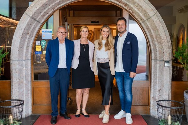 Eine Gruppe von vier Menschen posiert vor einem stilvollen Eingang, alle in eleganter Kleidung und mit freundlichen Gesichtsausdrücken.