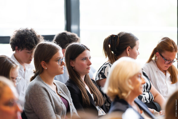A group of young adults attentively listening during a presentation, showcasing a mix of focused expressions and casual attire.
