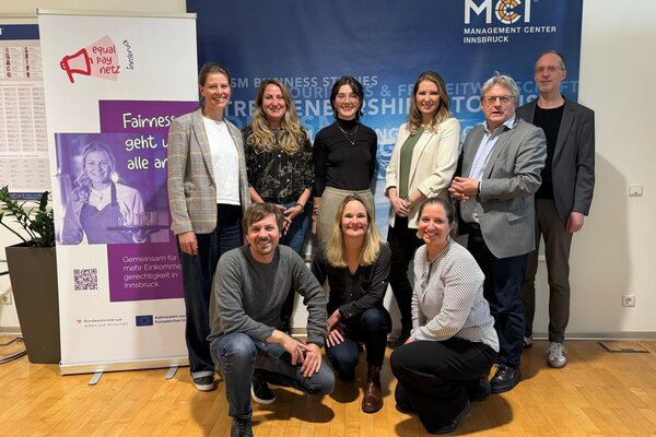 A diverse group of professionals poses together in a well-lit room, promoting equal pay and fairness in Innsbruck.